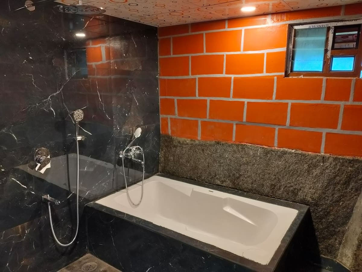 The bathroom, lined in dark marble against orange-painted brick, with a white bathtub and a wall-mounted shower.